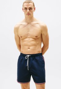 Bañadores de color navy con cintura ajustable, con franjas laterales en rojo y blanco. Fabricados en un tejido suave, de longitud a medio muslo, con un corte casual.