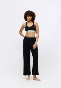 Μαύρο κοντό αθλητικό σουτιέν με πράσινες και λευκές ρίγες, συνδυασμένο με χαλαρές μαύρες φόρμες που διαθέτουν λογότυπο στη μέση.