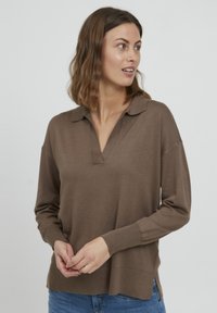 Pull brun à manches longues en tissu doux, doté d'un col polo, d'un léger décolleté en V et de fentes latérales à l'ourlet. Porté avec un jean.