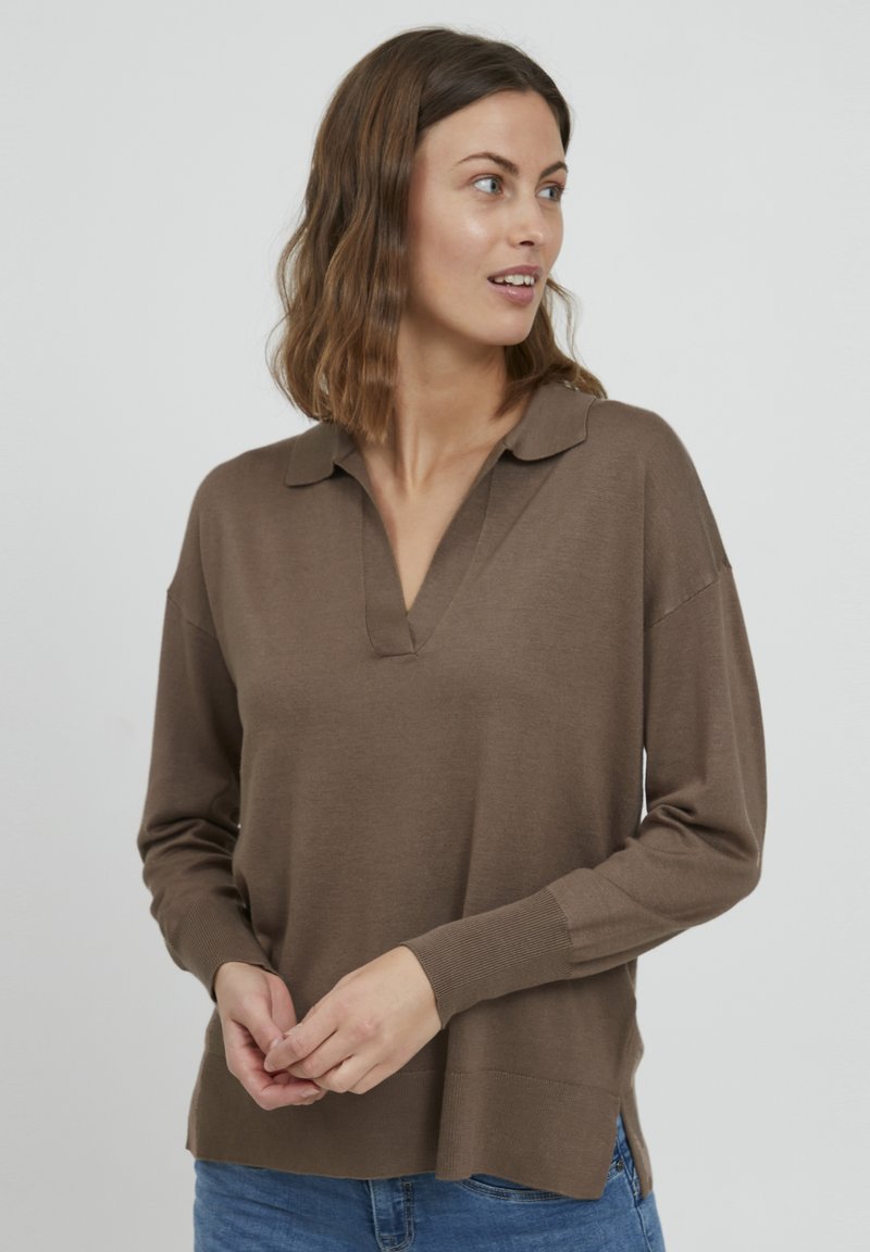Pull brun à manches longues en tissu doux, doté d'un col polo, d'un léger décolleté en V et de fentes latérales à l'ourlet. Porté avec un jean.