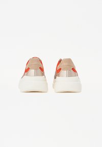 Sneakersy z beżową cholewką z zamszu i metalu, z pomarańczowymi akcentami i grubą białą podeszwą, zaprojektowane w zaokrąglonym kształcie.