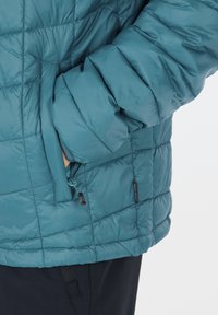 Teal isoleret jakke med quiltet design, lynlåslomme og struktureret stof. Inkluderer mørke accenter og en afslappet pasform.