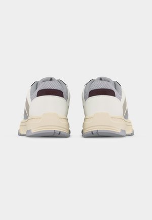 Paire de chaussures de sport blanches et grises avec des semelles beiges, vues de dos sur un fond blanc uni.