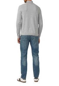 Szary sweter z dzianiny z kołnierzem, zestawiony z jasnoniebieskimi dżinsami. Białe trampki z ciemnymi akcentami. Widok od tyłu.
