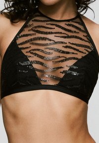 Bralette negra con un escote alto, malla transparente con patrones de lentejuelas ondulados y una banda suave en la parte inferior.