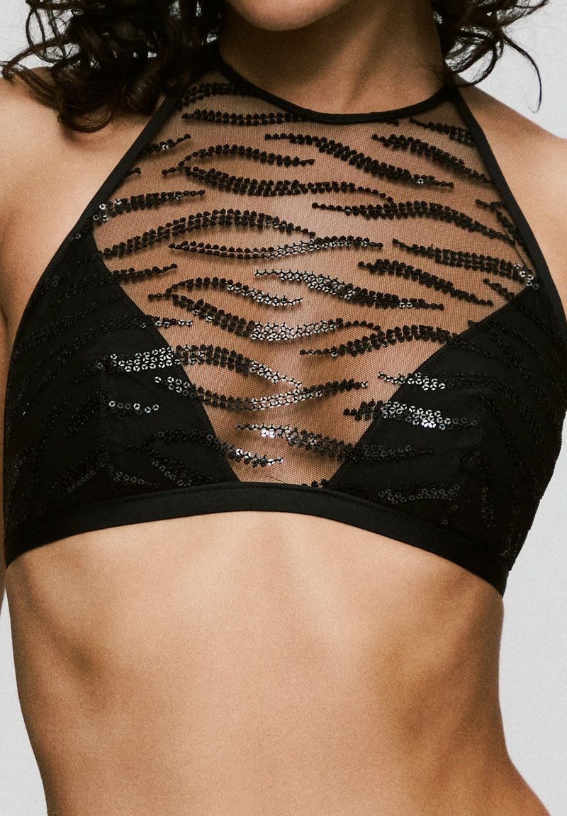 Bralette negra con un escote alto, malla transparente con patrones de lentejuelas ondulados y una banda suave en la parte inferior.