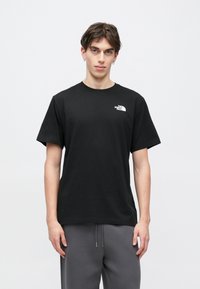 Μαύρο βαμβακερό t-shirt με στρογγυλή λαιμόκοψη και κοντά μανίκια. Φέρει λευκό λογότυπο στο αριστερό στήθος. Το μοντέλο φορά γκρι παντελόνια.