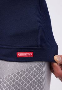 Marine thermoshirt met gestructureerde stof, geribbelde accenten en een rood label met de tekst "THERMOLACTYL 3." Grijze onderhemd met zichtbaar ruitpatroon.