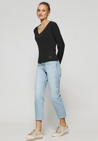 Svart långärmad V-ringad topp i kombination med ljusblå cropped jeans och beige sneakers, med en diskret logotypdetalj vid fållen.