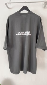 Gray oversized t-shirt with a round neck, featuring bold white text on the back that reads "DON'T FEAR THE UNKNOWN" and a web URL.