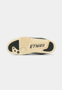 Black sneaker sole with a textured rubber surface, featuring a cream-colored midsole with "ETNIES" logo and distinct traction patterns.