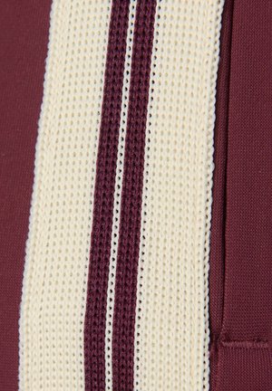 Bordeauxrode sportstof met een witte, gestructureerde streep met drie smalle, gebreide secties, vergezeld van fijne stiksels langs de randen.