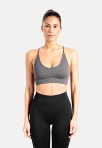 Grijs sportbeha met een ronde hals en dunne bandjes. Zachte stof met een gladde textuur. Draagt bij hoge taille zwarte leggings.