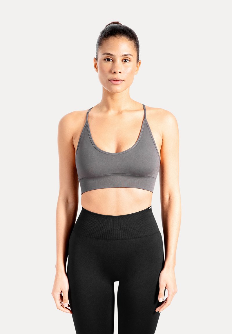 Grijs sportbeha met een ronde hals en dunne bandjes. Zachte stof met een gladde textuur. Draagt bij hoge taille zwarte leggings.