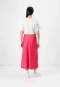 Jupe maxi satin fuchsia avec une texture lisse et longueur cheville, associée à un t-shirt à manches courtes gris clair et des chaussures blanches.
