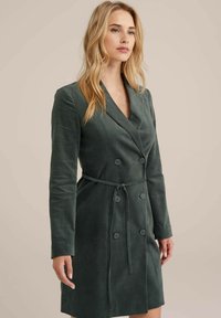 Caban dublu, de culoare verde închis, realizat dintr-un material moale, cu curea în talie, mâneci lungi și rever cu notch; textură netedă.