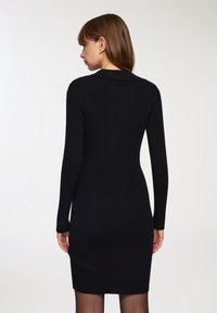 Abito nero a coste con maniche lunghe, design aderente e colletto alto. Tessuto liscio, lunghezza al ginocchio e senza motivi o dettagli visibili.