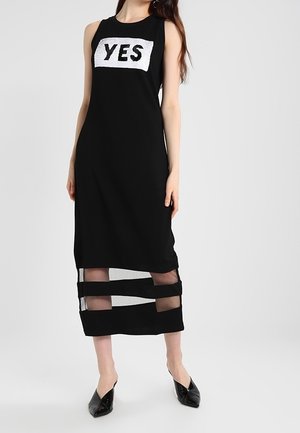 Robe noire sans manches avec un motif "YES" en sequins blancs, présentant des découpes à rayures en maille au niveau de l'ourlet et une silhouette ajustée.