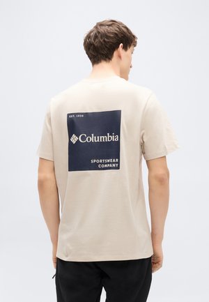 Beige bomuld T-shirt med en marineblå firkantet logo med teksten "Columbia" og "Sportswear Company" på bagsiden. Korte ærmer, almindelig pasform.