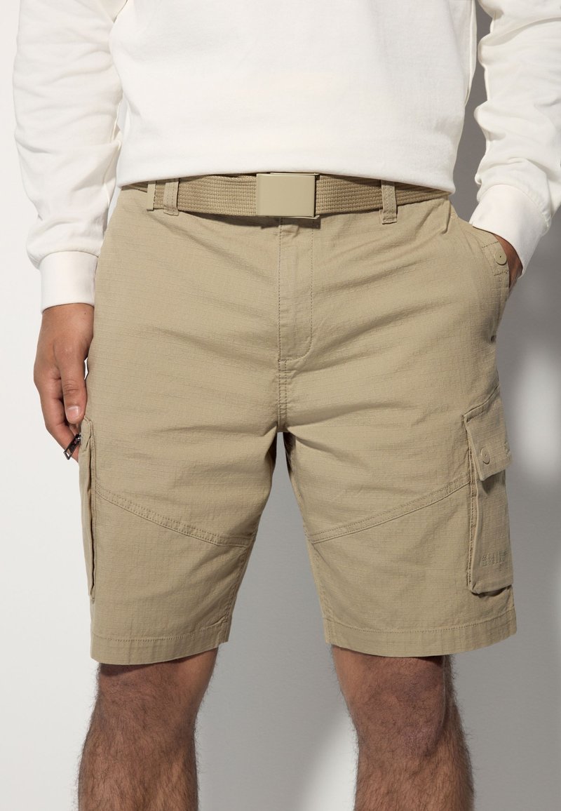 Khaki cargo shorts with a textured design, featuring side pockets and a flat waistband with a matching belt.