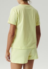 Jasnożółta bawełniana koszulka z podwiniętymi rękawami, w zestawie z dopasowanymi szortami. Prosty fason, miękka tekstura i brak wyraźnych wzorów lub akcentów.
