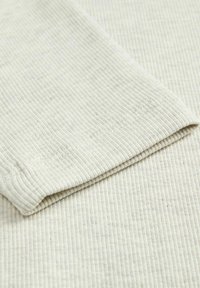 Lys beige ribbet stoff med en myk tekstur, med en brettet kant og subtile nupper for ekstra detaljer. Egnet for casual bruk.