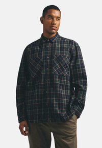 Koszula flanelowa w kratę w ciemnym niebieskim, zielonym i burgundowym kolorze. Posiada zapięcie na guziki z przodu, kołnierzyk oraz dwie kieszenie na piersi. Miękka faktura.