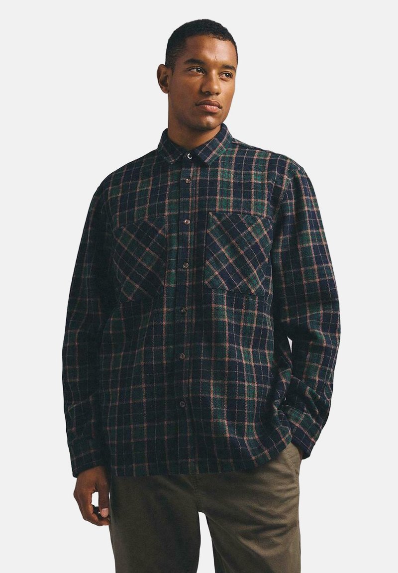 Koszula flanelowa w kratę w ciemnym niebieskim, zielonym i burgundowym kolorze. Posiada zapięcie na guziki z przodu, kołnierzyk oraz dwie kieszenie na piersi. Miękka faktura.