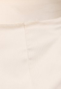 Textura de tela beige con un acabado suave y un brillo sutil. Presenta una costura limpia a lo largo del borde, destacando la durabilidad del material.