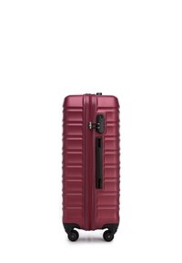 Valigia rigida in vinile di colore bordeaux, con un design a righe, cerniere nere, una maniglia laterale e quattro ruote nere per la mobilità.