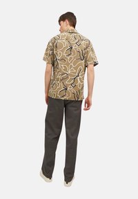 Chemise marron à manches courtes avec un motif abstrait blanc et marine, associée à un pantalon gris. La chemise est dotée d'un col camp et d'une coupe décontractée.