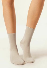 Calcetines de algodón beige de corte crew con una textura suave y puños acanalados, que terminan justo por encima del tobillo, presentados sobre piernas descubiertas.