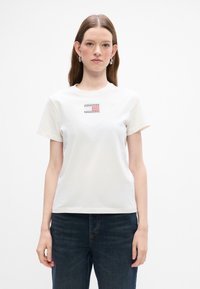 Hvid bomulds t-shirt med korte ærmer og rund halsudskæring, med et lille farvet grafisk design foran på midten.