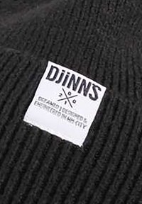 Gorro de punto negro con canalé texturizado. Presenta una etiqueta blanca con "DJINNS" y texto adicional, indicando la marca y el origen del diseño.