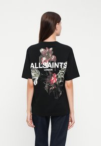 T-shirt grafica nera con design floreale dai colori vivaci e catene, con "ALLSAINTS LONDON" stampato in bold lettere bianche.