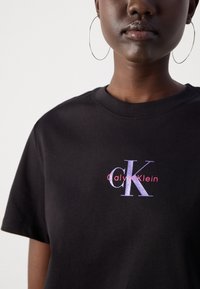 Fekete pamut póló kerek nyakkal, rövid ujjakkal, színes "CK" logóval a mellkason, alatta a "Calvin Klein" felirattal.