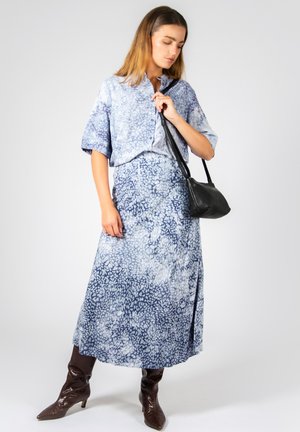 Blusa a maniche corte blu e bianca con motivo, abbinata a una lunga gonna coordinata. Una borsa a tracolla nera e stivali marroni fino al ginocchio completano il look.