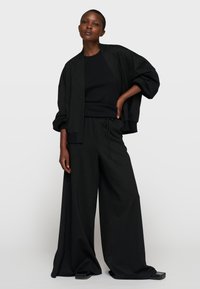 Conjunto de punto negro texturizado que incluye una chaqueta crop suelta con mangas anchas y pantalones relajados con cintura ajustable mediante cordón. Acabado con un brillo sutil.