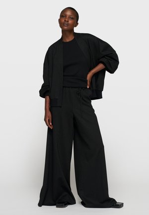 Completo in maglia nera con texture, composto da giacca corta ampia con maniche larghe e pantaloni comodi con vita con coulisse. Accentuato da una sottile brillantezza.