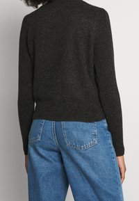 Dunkelgrauer gestrickter Pullover mit hohem Kragen und langen Ärmeln, kombiniert mit hellblauen Jeans aus Denim mit Gesäßtaschen.