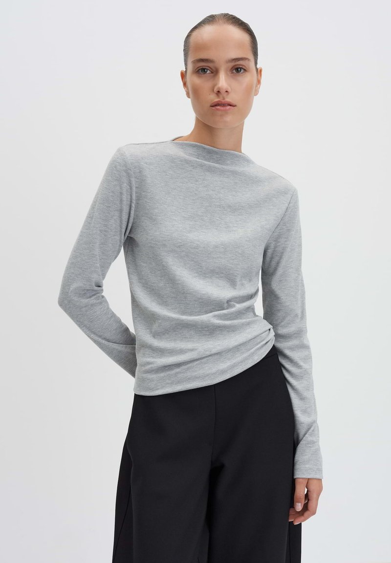 Maglietta grigia a maniche lunghe in tessuto a costine con scollatura a barca, abbinata a pantaloni neri a vita alta. Design semplice e aderente.
