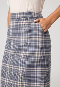 Jupe à carreaux en mélange de laine avec un motif bleu et crème, taille haute et détails de poches latérales. Texture lisse et coupe ajustée.