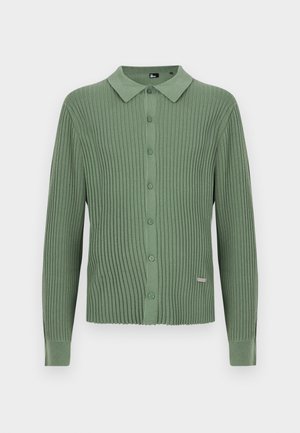 Grønn ribbestrikket cardigan med lange ermer, krage og knapping foran, med et lite metallmerke nær kanten.