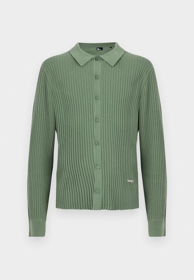 Πράσινη ριγωτή πλεκτή μπλούζα με μακρύ μανίκι, γιακά και κλείσιμο μπροστά με κουμπιά, με μικρή μεταλλική ταμπέλα бренда κοντά στο τελείωμα.