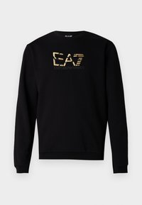 Svart genser laget av mykt stoff med rund hals og lange ermer, pyntet med en gullfarget logodesign på brystet.