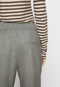 Gray herringbone trousers with an elastic waistband, paired with a brown and cream striped long-sleeve top. Features a single back pocket.