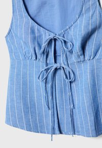 Světle modrý, bez rukávů, top s bílými vertikálními pruhy. Obsahuje kulatý výstřih vzadu a zavazování v přední části. Měkká, texturovaná tkanina.