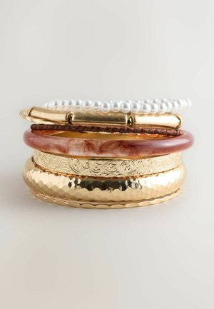 Set of stacked bracelets including hammered gold, engraved gold, marbled brown, and a pearl strand, featuring varied textures and shapes.