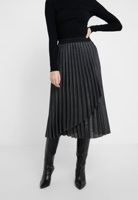 Falda midi plisada en tejido gris oscuro con un ligero brillo. Presenta un dobladillo asimétrico y una cinturilla negra con marca. Combinada con botas altas negras.