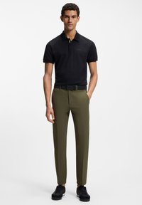 Czarna teksturowana koszulka polo z kołnierzykiem, zestawiona z dopasowanymi oliwkowozielonymi spodniami i czarnymi tenisówkami, z czarnym paskiem.